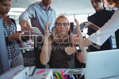 Irritated businesswoman sitting amidst team holding technologies