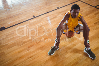 Thoughtful teenage player sitting on basketball