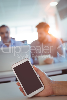 Cropped hand of business person holding smartphone on desk