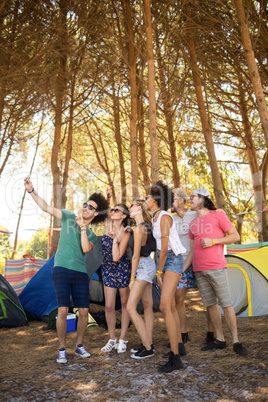 Full length of cheerful friends taking selfie at campsite