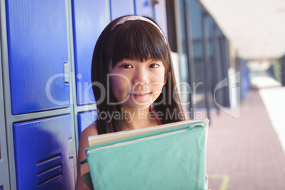 Portrait of elementary schoolgirl holding books in corridor
