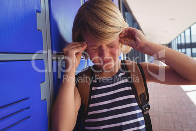 Schoolboy suffering from headache while standing by lockers