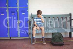 Full length of sad boy sitting on bench by lockers