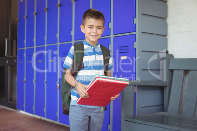 Portrait of smiling boy holding books in corridor