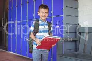 Portrait of smiling boy holding books in corridor