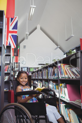Smiling girl with book on wheelchair in library
