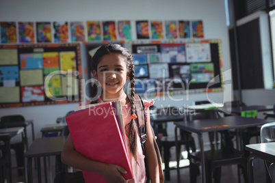 Girl holding books while standing in classroom