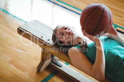 Portrait of woman with basketball lying on bench in court