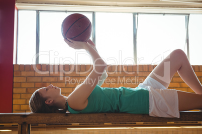 Woman playing with basketball while lying on bench in court