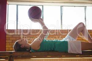 Woman playing with basketball while lying on bench in court