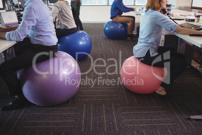 Low section of business people sitting on exercise balls while working at office