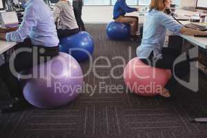 Low section of business people sitting on exercise balls while working at office