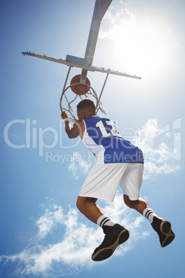 Rear view of male teenager hanging on basketball hoop