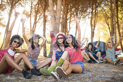 Cheerful friends with arm raised sitting at campsite