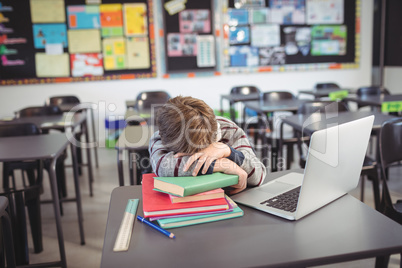 Tired schoolboy sleeping on stack of in classroom