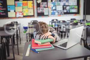Tired schoolboy sleeping on stack of in classroom