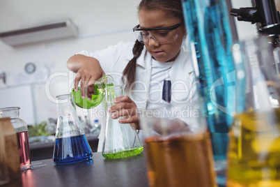 Elementary student pouring green chemical in flask at laboratory