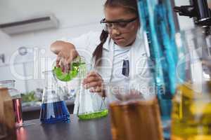 Elementary student pouring green chemical in flask at laboratory