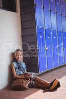 Portrait of elementary student using mobile phone while sitting by lockers