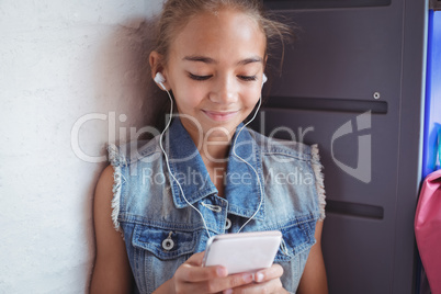 Elementary schoolgirl using mobile phone by wall