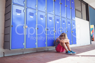 Full length of schoolgirl sitting by lockers in corridor