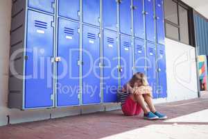 Full length of schoolgirl sitting by lockers in corridor