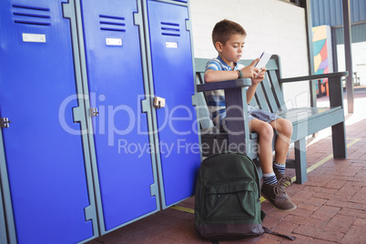 Boy using mobile phone while sitting on bench by lockers