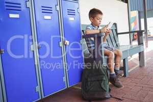 Boy using mobile phone while sitting on bench by lockers