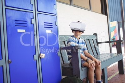 Boy using virtual reality glasses while sitting on bench by lockers
