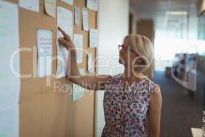 Businesswoman reading paper on notice board