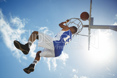 Low angle view of male teenager hanging on basketball hoop