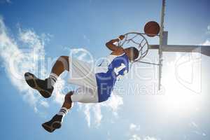 Low angle view of male teenager hanging on basketball hoop