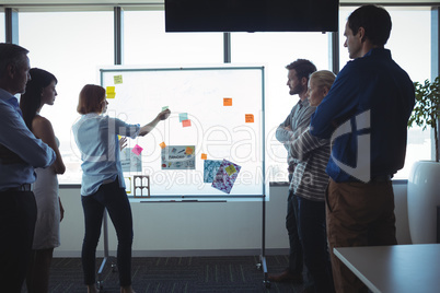 Businesswoman sticking adhesive notes on whiteboard while colleagues standing at office