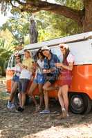 Full length of fiends using mobile phone while standing by camper van