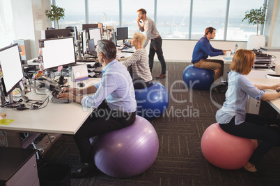 Business people sitting on exercise balls while working in office