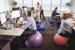 Business people sitting on exercise balls while working in office
