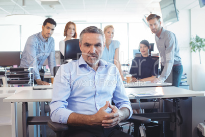 Portrait of serious businessman with team in background