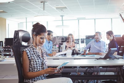 Young businesswoman using digital tablet while colleagues discussing in office