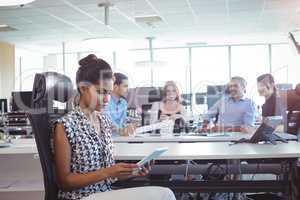 Young businesswoman using digital tablet while colleagues discussing in office