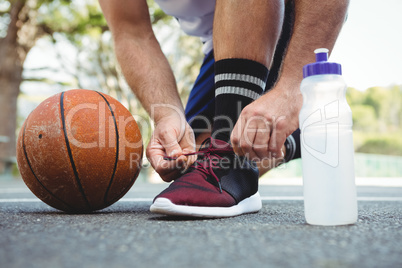 Low section of basketball player tying shoelace