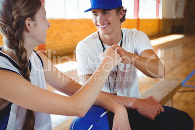 Smiling coach doing fist bump with female basketball player