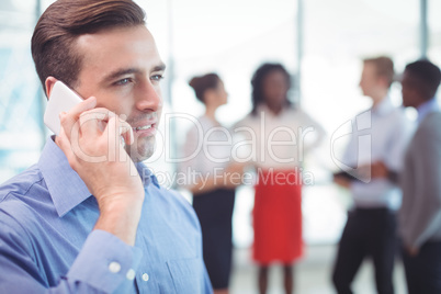 Businessman talking on mobile phone with colleagues discussing in background