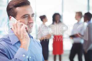 Businessman talking on mobile phone with colleagues discussing in background