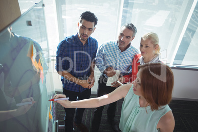 High angle view of businesswoman explaining to colleagues over whiteboard