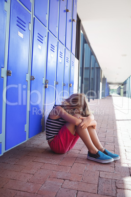 Full length of girl sitting by lockers in corridor