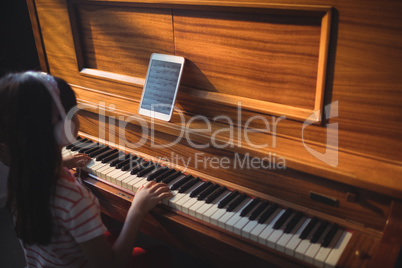 High angle view of girl wearing headphones while practicing piano in classroom