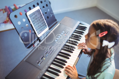 Elementary girl looking at digital tablet on stand while practicing piano