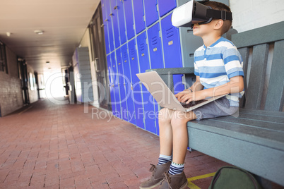 Boy using laptop and virtual reality glasses while sitting on bench in corridor