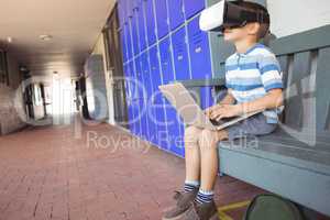 Boy using laptop and virtual reality glasses while sitting on bench in corridor