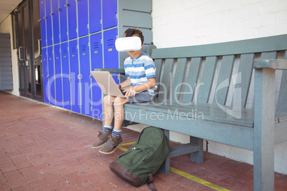 Full length of boy using laptop and virtual reality glasses while sitting on bench
